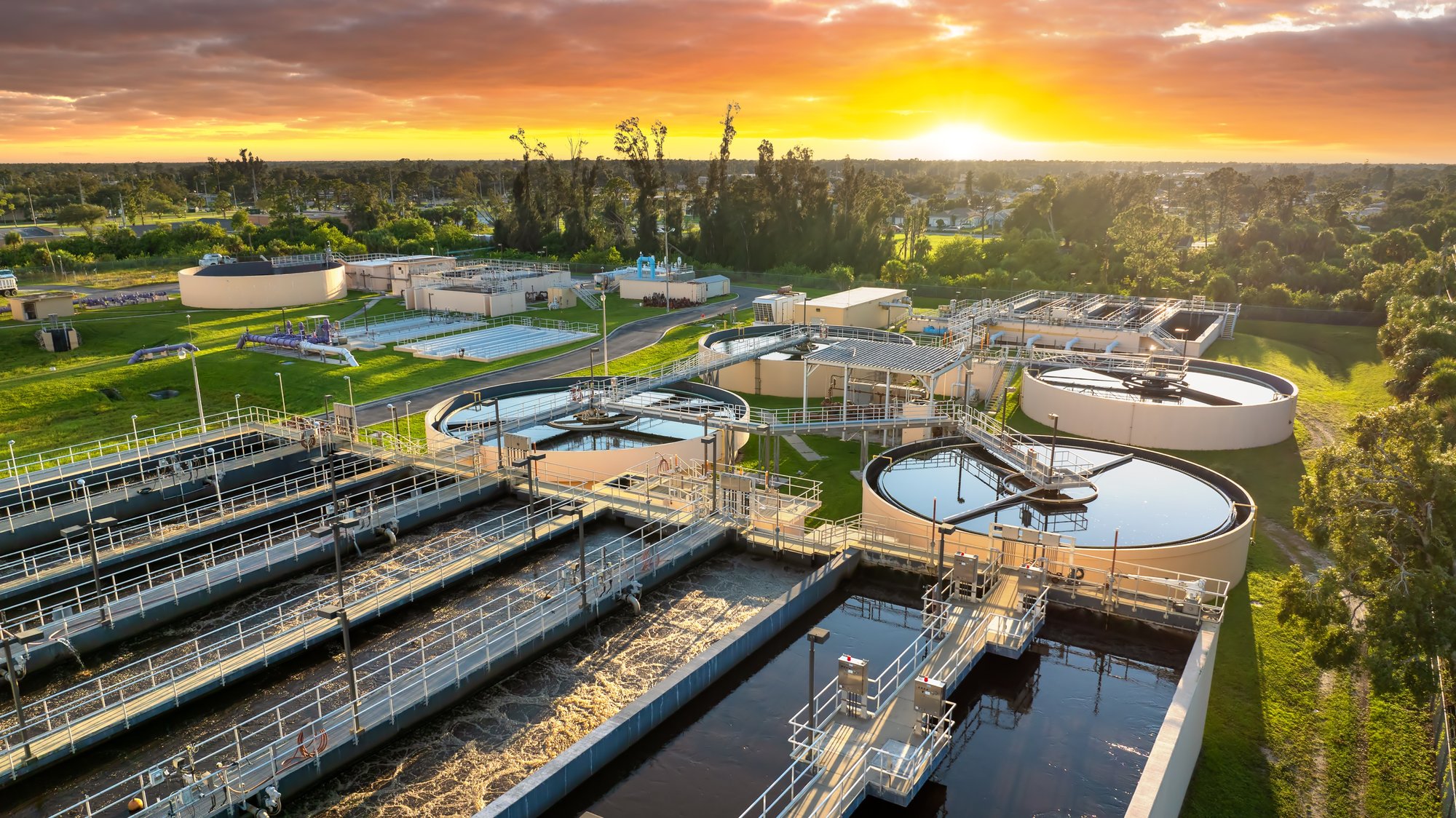 Aerial view of a water and wastewater treatment facility at sunset, showing clarifiers, aeration basins, and interconnected treatment infrastructure surrounded by landscaped grounds.