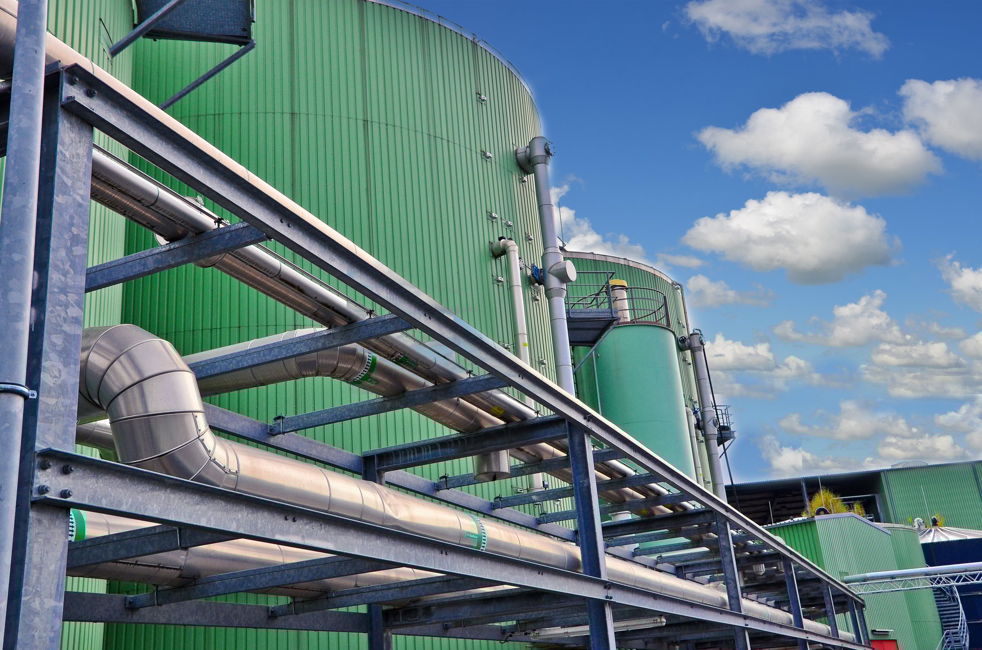 Anaerobic digesters at a wastewater treatment facility with green tanks and exposed piping used for biogas capture and energy recovery.