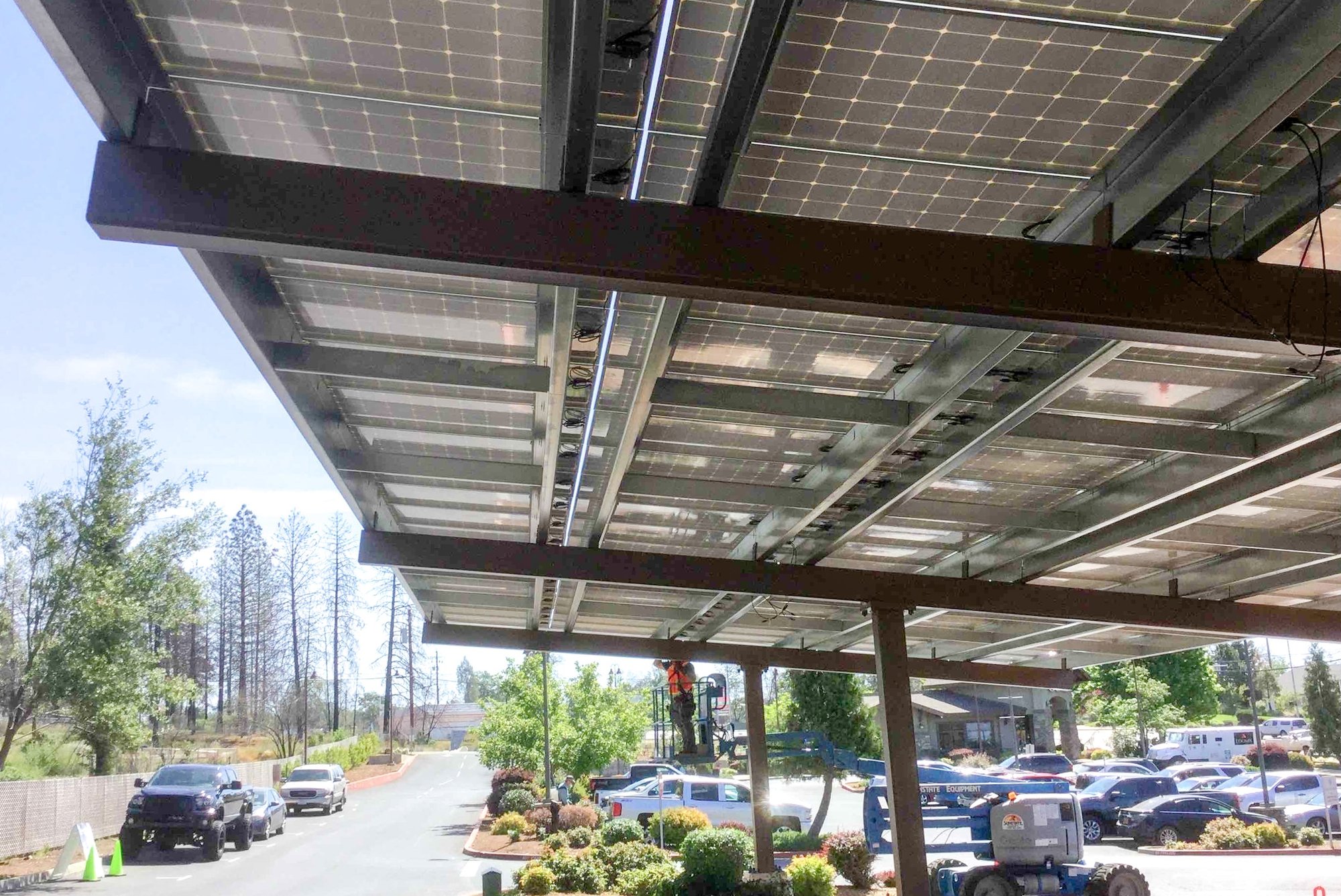 Solar panels installed on a parking canopy as a worker performs maintenance below, providing on-site renewable energy for a healthcare campus parking area.