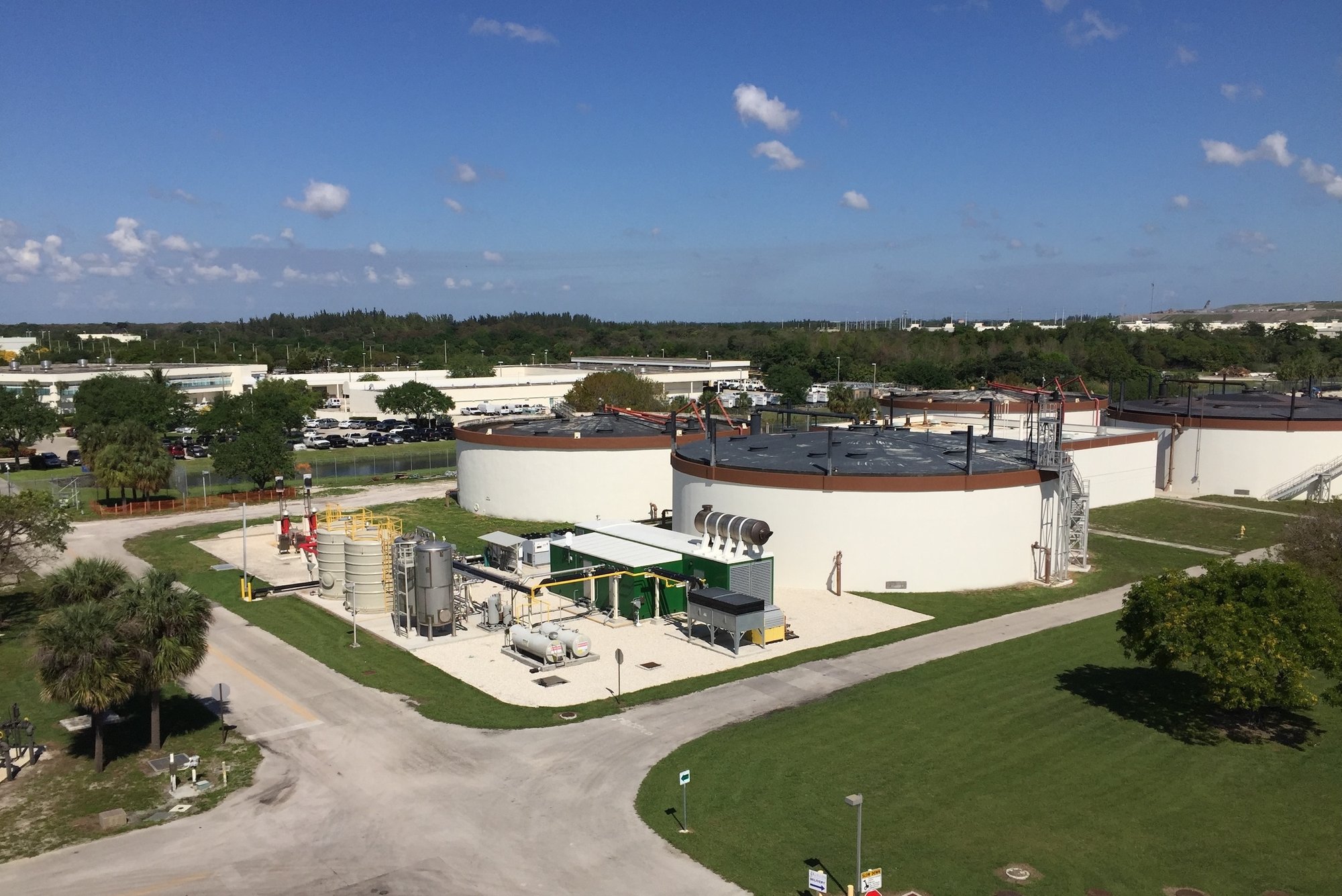 Aerial view of a Broward County wastewater treatment plant featuring large circular tanks and an adjacent cogeneration facility with industrial equipment and piping.