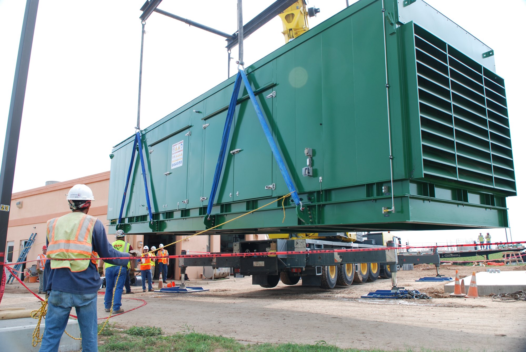 Heavy industrial equipment being lifted into place at an active infrastructure site, with construction crews coordinating a large-scale energy system installation to support reliable operations.