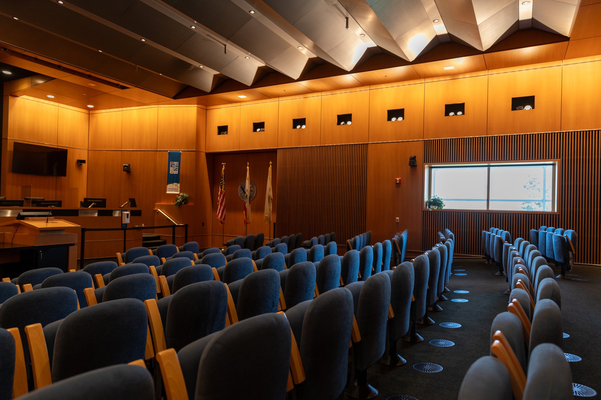 Interior of City of Milpitas council chamber showcasing upgraded lighting, wood-paneled walls, and tiered seating for public meetings.