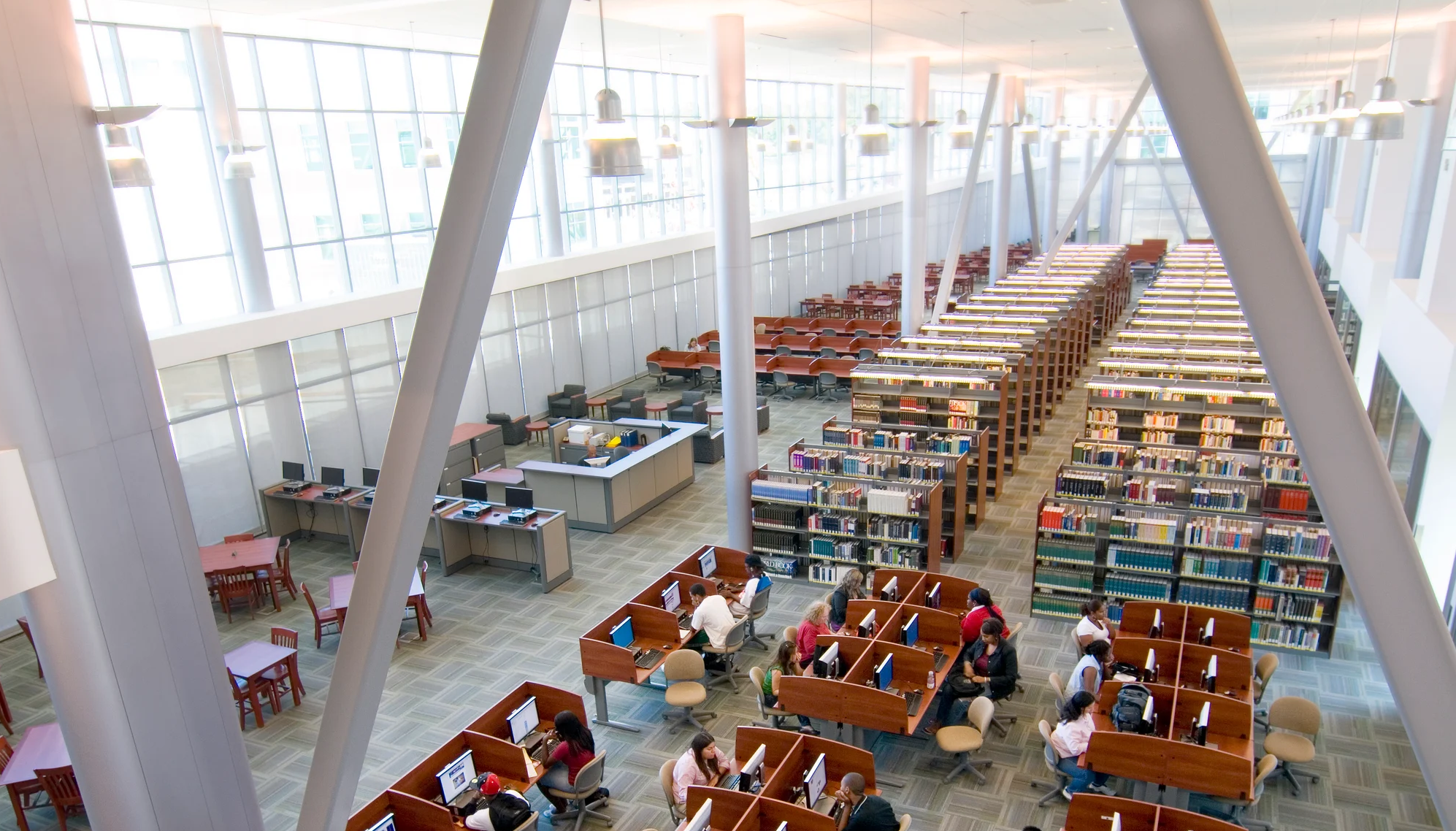 Brightly lit library interior at Contra Costa Community College featuring upgraded lighting fixtures above study tables, computer stations, and book stacks as part of a campus-wide lighting retrofit project.