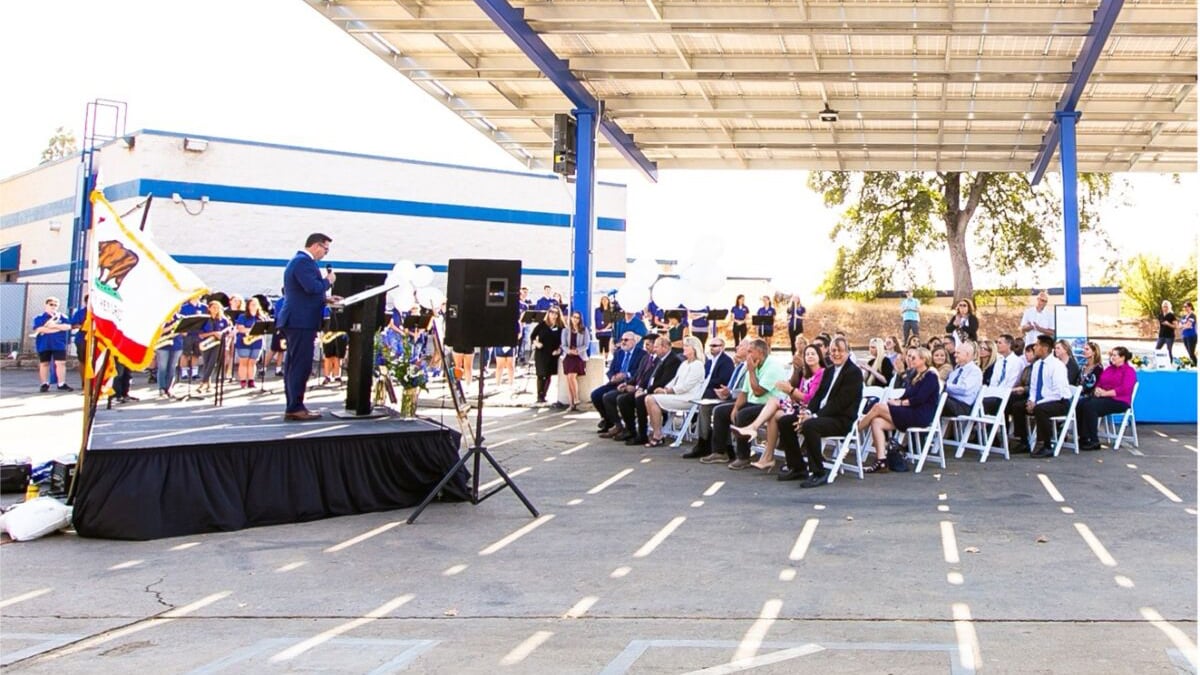 Dedication ceremony at an El Dorado USD school, with attendees seated beneath a solar carport as speakers address the crowd.