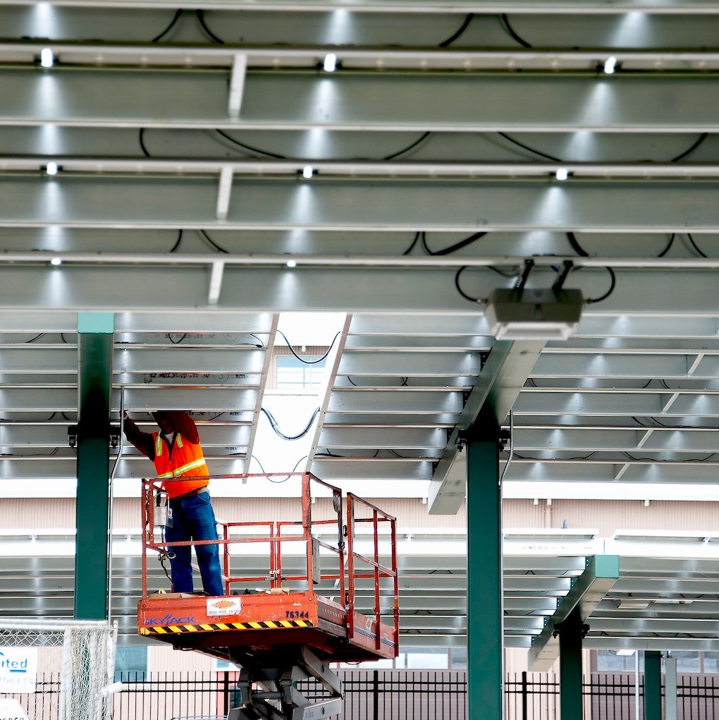 Technician performing maintenance work beneath a solar canopy structure at Hartnell College, illustrating ongoing system monitoring and operational support.