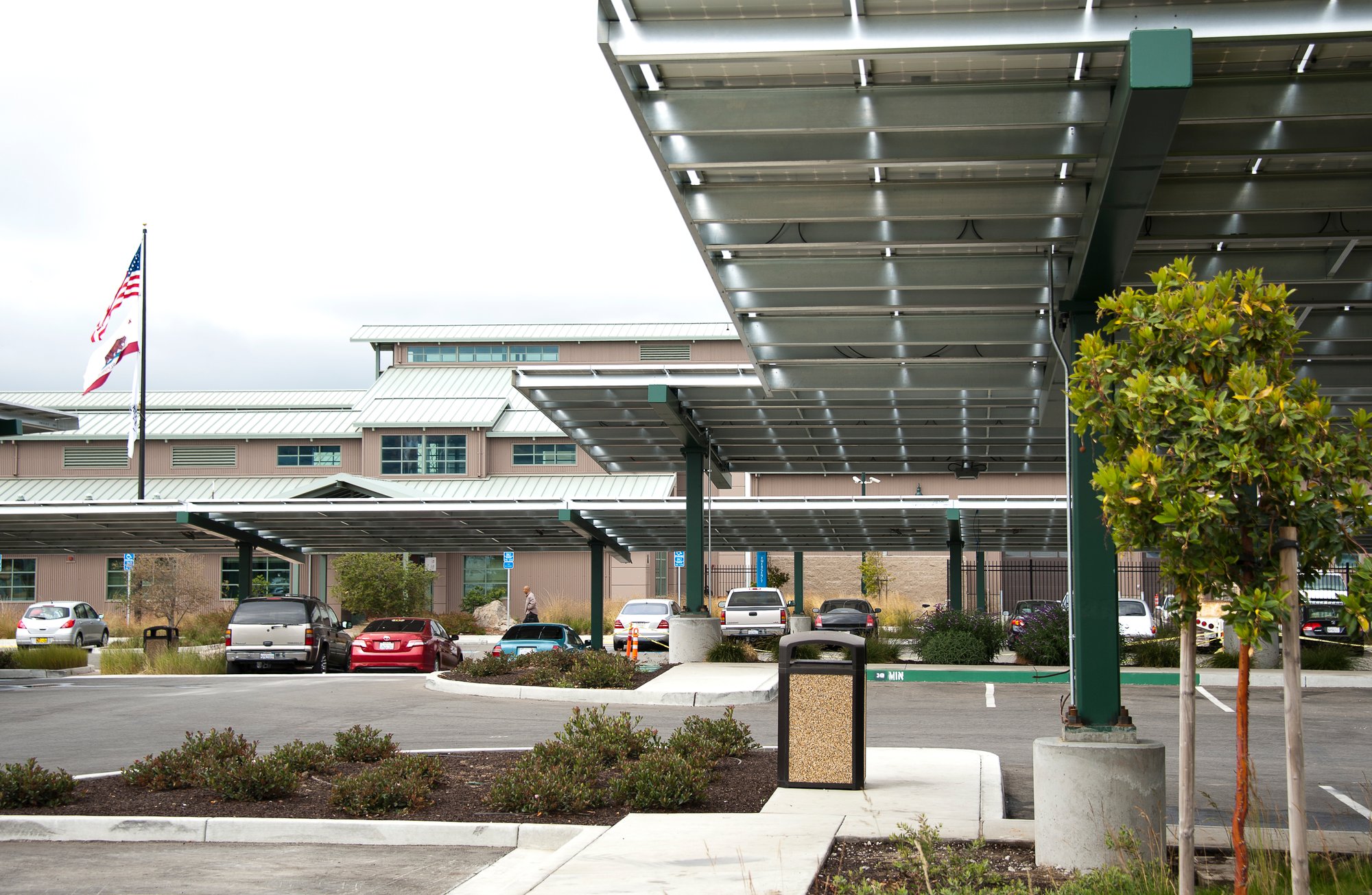 Modern campus building and covered walkway at Hartnell College featuring solar canopy structures, landscaped grounds, and American flag in the background.