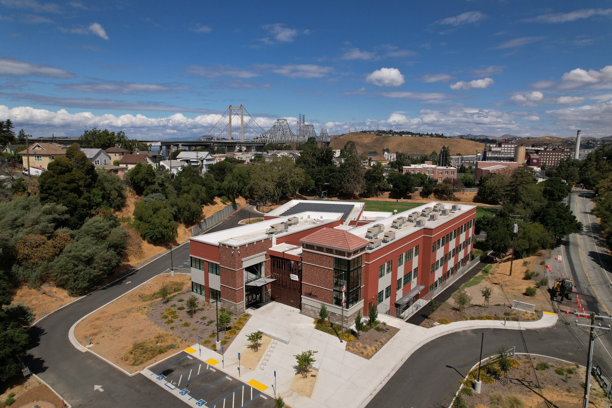 Aerial view of John Swett USD middle school campus featuring a modern red-brick building with rooftop solar panels and a suspension bridge in the background.
