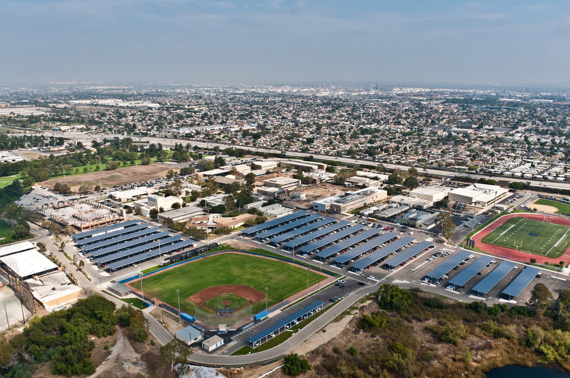 Aerial view of Los Angeles County Community College District campus featuring extensive rooftop and parking lot solar installations, athletic fields, and surrounding urban landscape.