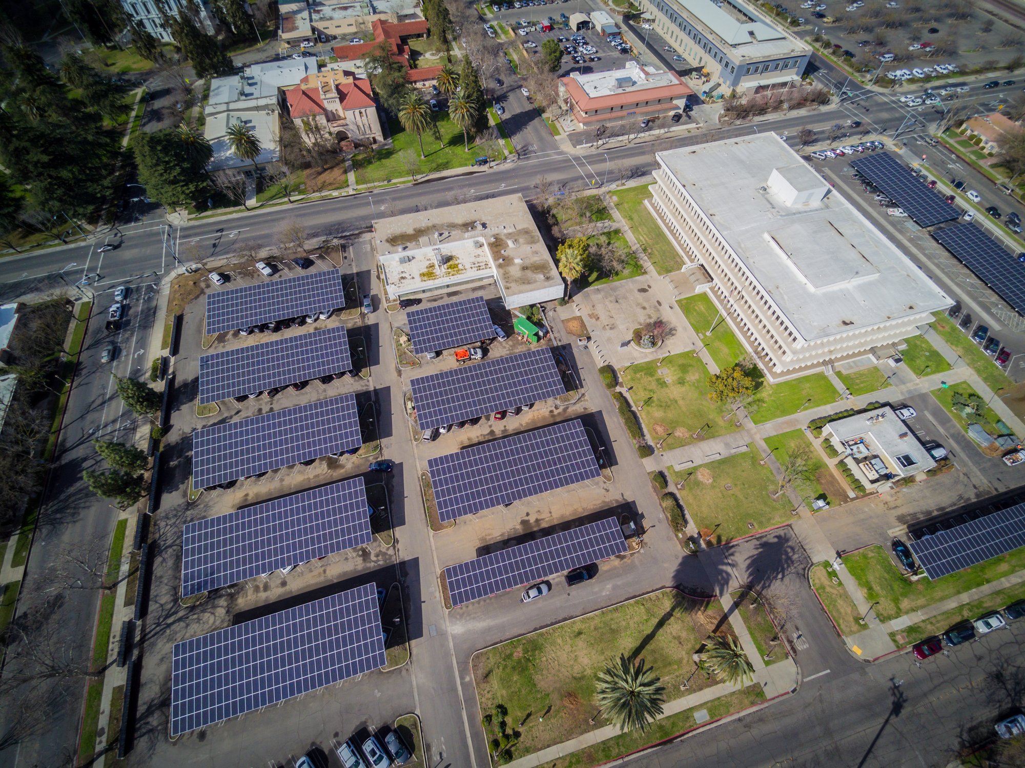 Aerial view of a county government complex with multiple solar carport installations covering parking areas, adjacent to administrative buildings and landscaped grounds.