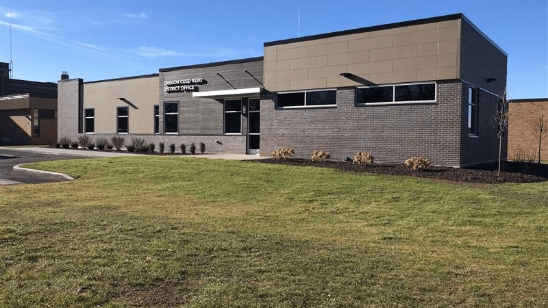 Exterior view of the Oregon CUSD 220 district office building, featuring a modern brick and panel design with landscaped grounds.