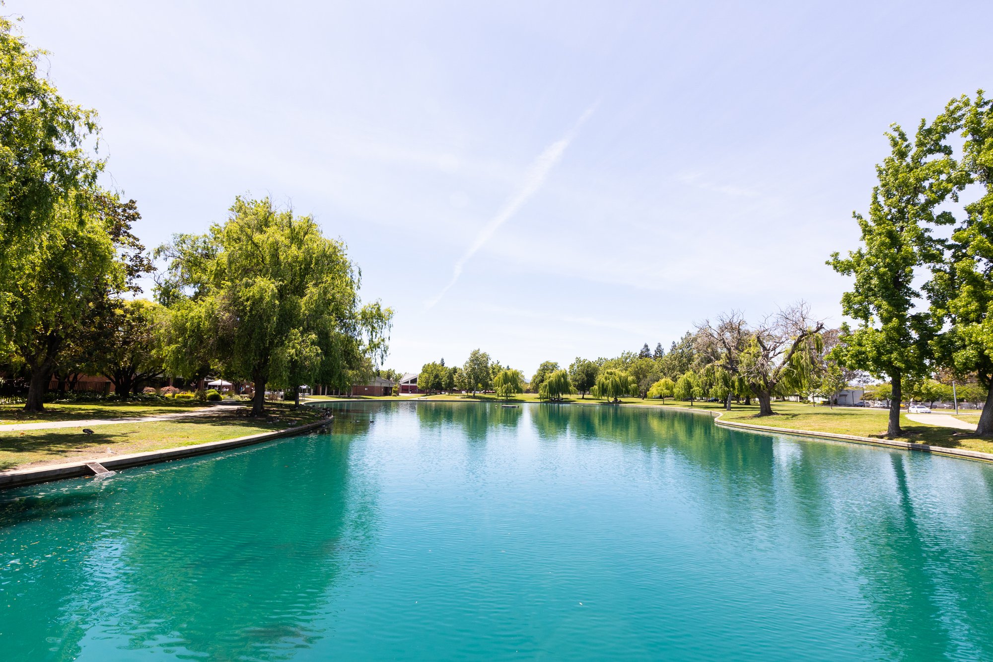 Scenic view of a landscaped park in Solano County featuring a calm pond surrounded by trees, walking paths, and open green space under a clear sky.