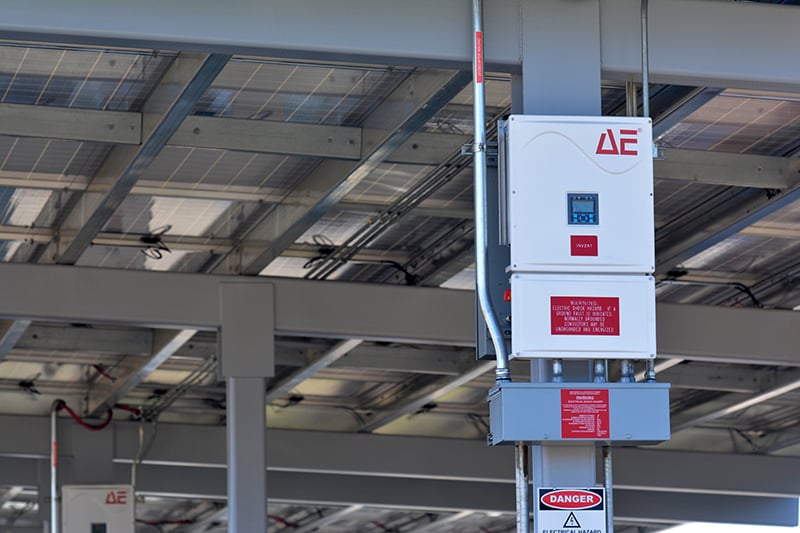 Modern electrical inverter and distribution equipment installed beneath a solar canopy structure at a school facility.