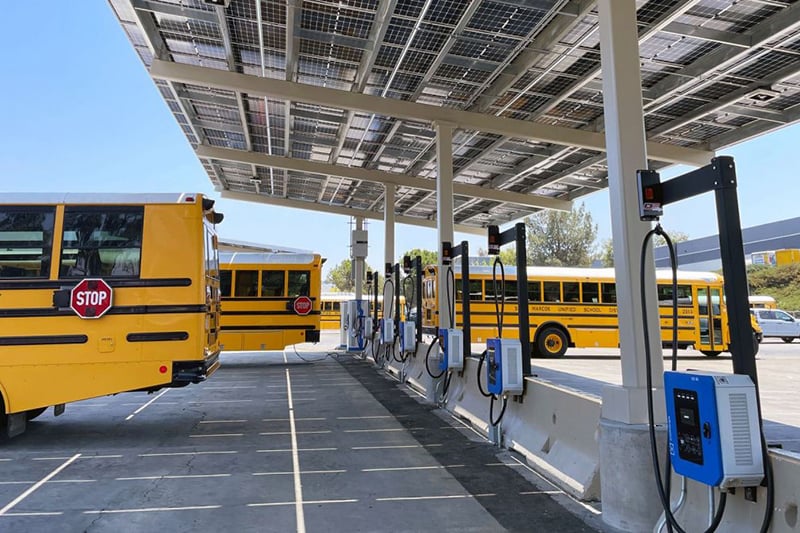 Electric school buses charging at a solar-powered fleet depot equipped with EV charging infrastructure.