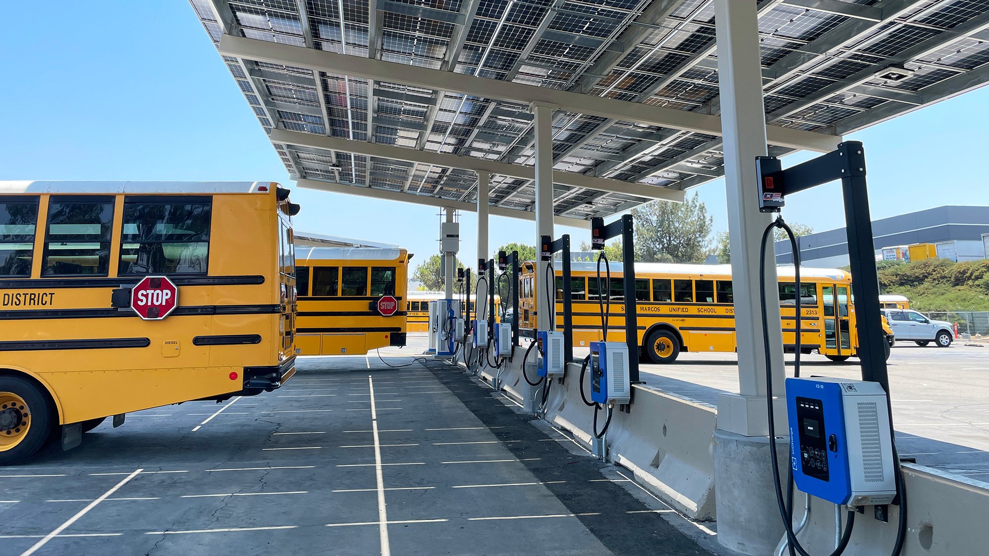 Electric school buses charging at a fleet depot equipped with solar canopies and EV charging infrastructure.