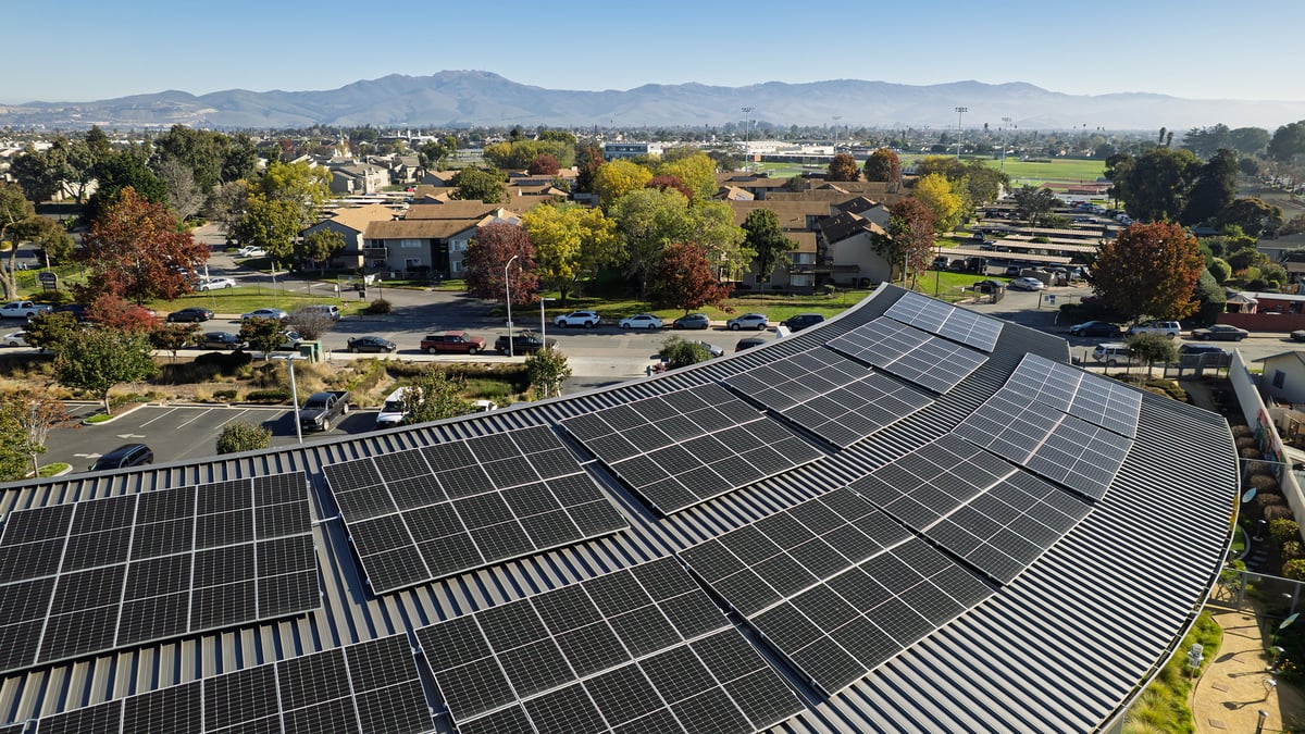Aerial view of a large solar panel array in Salinas, CA, with neighborhoods, trees, and hills in the distance.