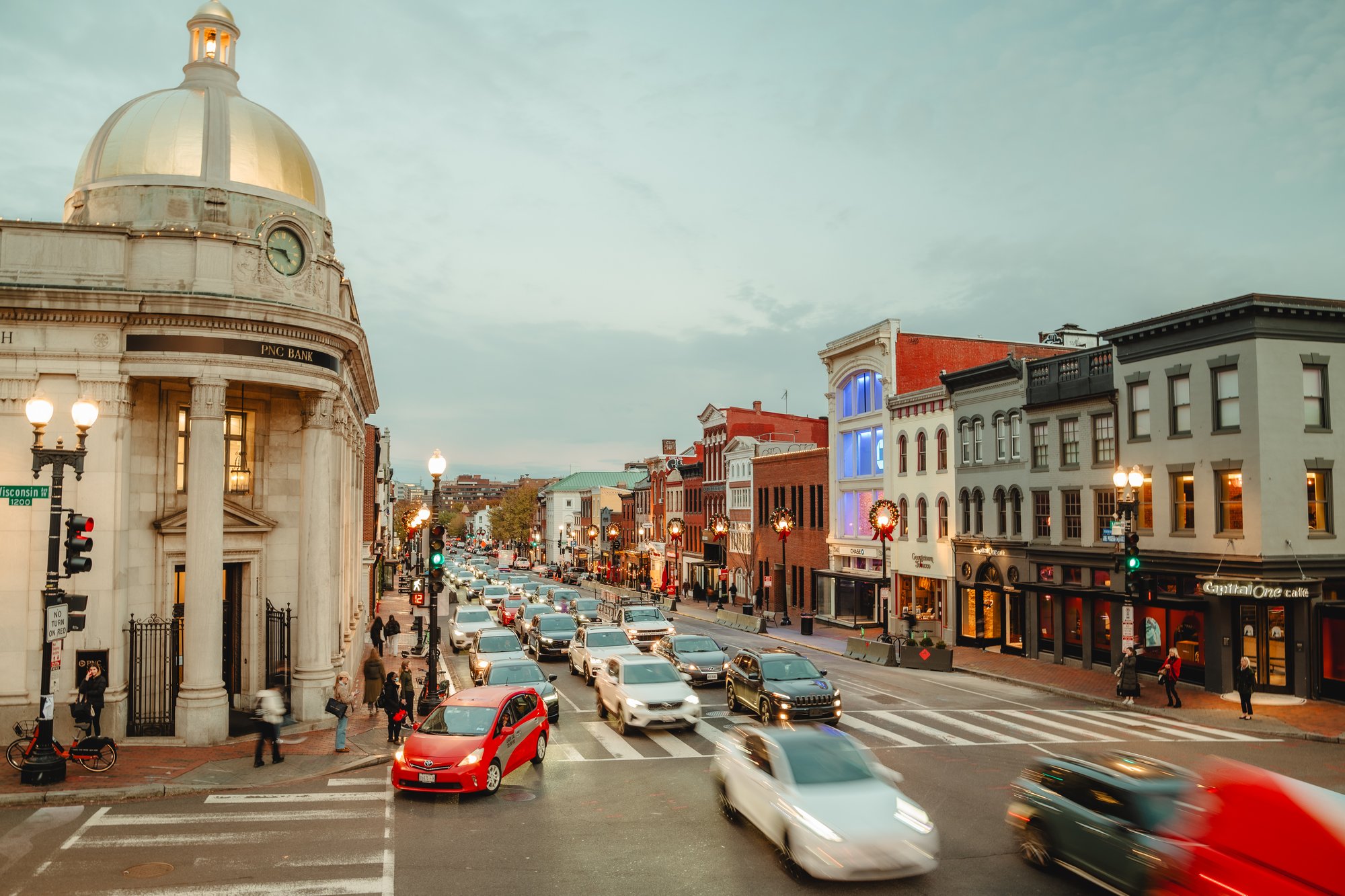 Evening street scene in Washington, DC featuring illuminated historic buildings, active traffic, and upgraded street lighting along a busy downtown corridor.