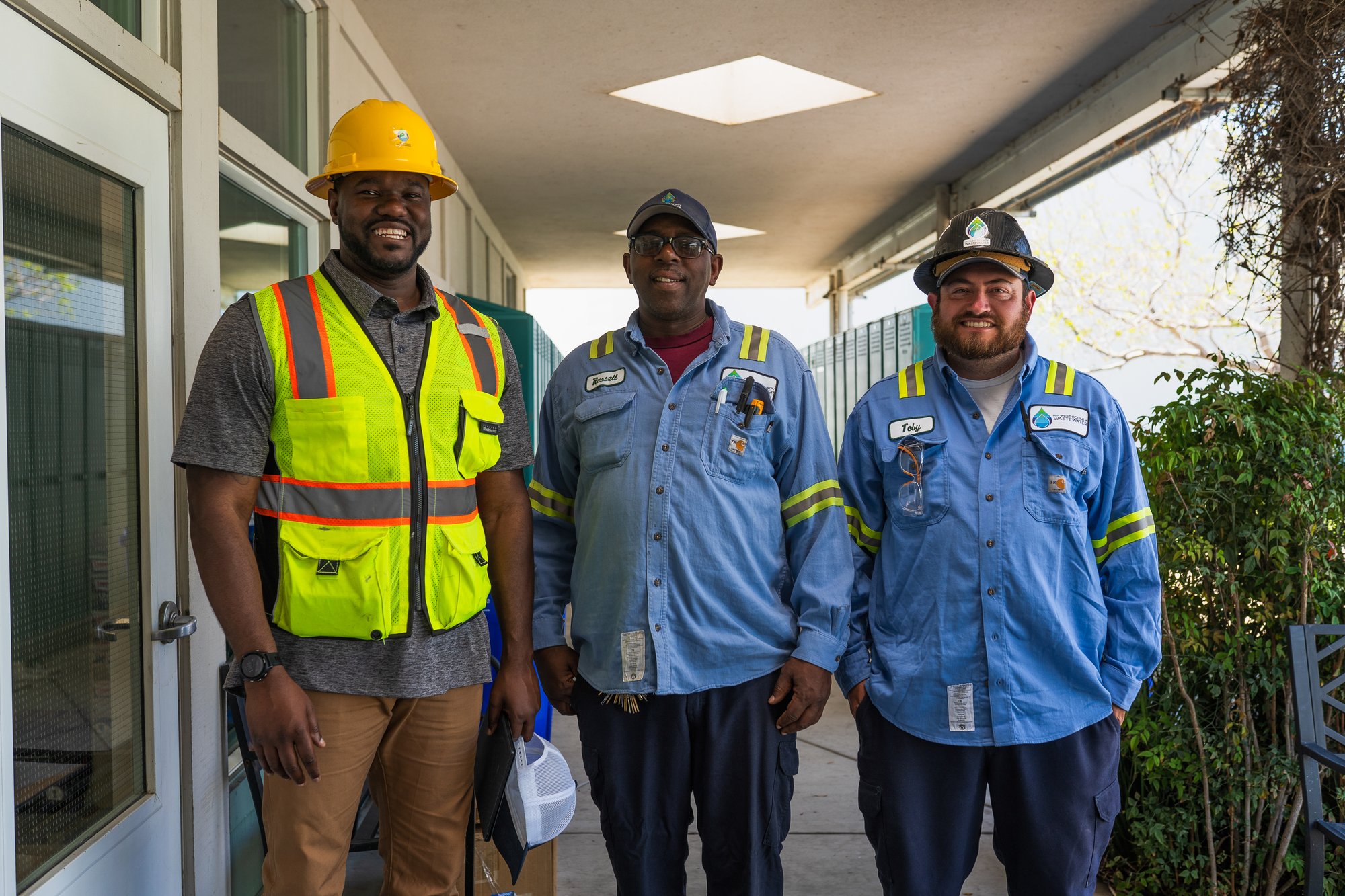 Operations and maintenance employees wearing safety gear and uniforms stand together at a project site.
