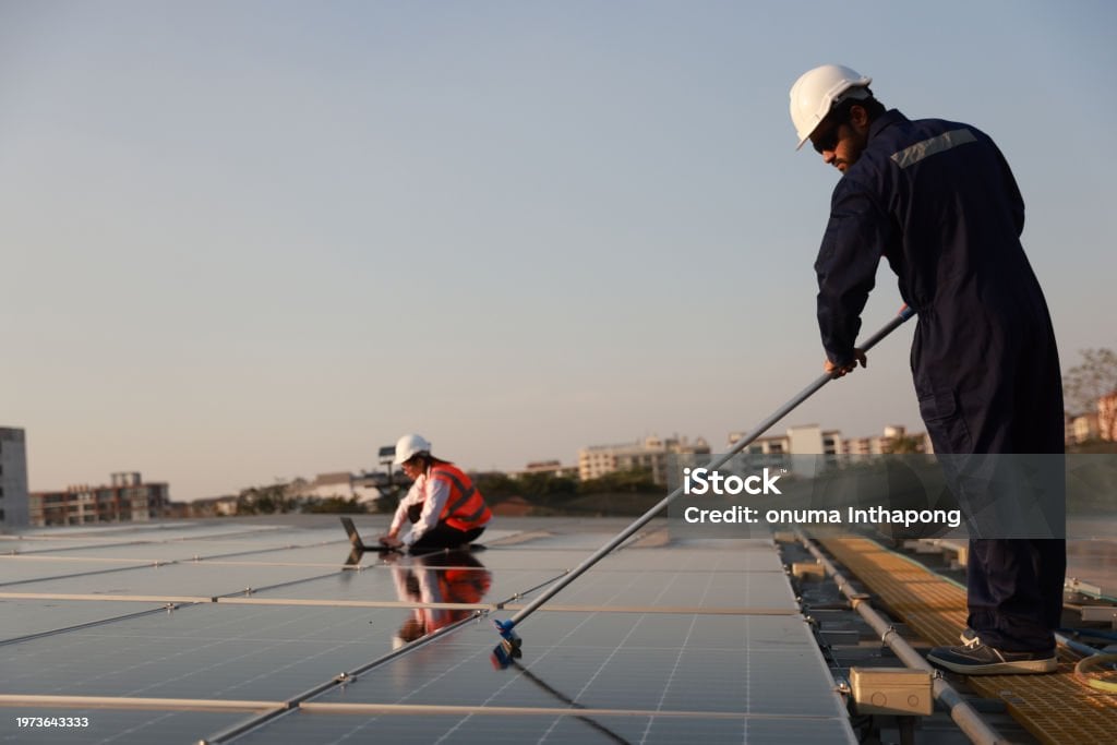 Workers in safety gear clean and inspect rooftop solar panels at an active commercial facility, supporting reliable on-site energy performance.